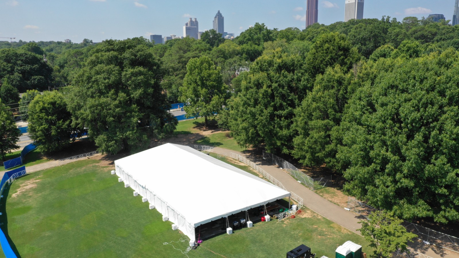 Aerial view of a white clearspan structure tent on a grassy park lawn with the Atlanta skyline behind the trees